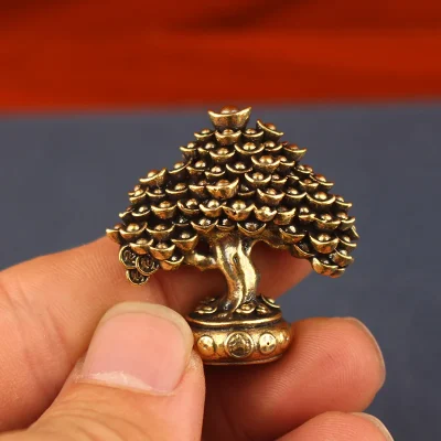 Small brass money tree held between thumb and finger, showing its size