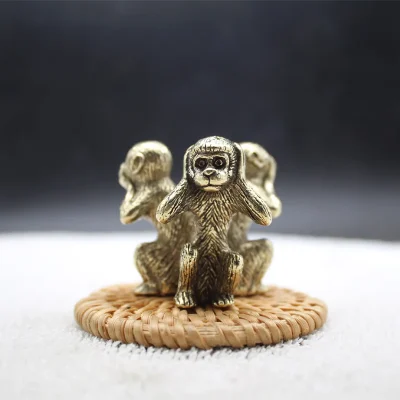 Three wise monkeys in copper sitting in a row on a woven mat